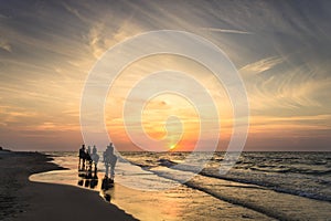 Riders on horseback riding along the seashore at sunset