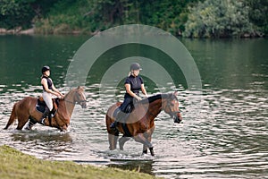 Riders, two young women riding horses down the river