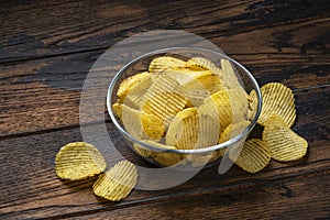 Ridged potato chips in bowl on wooden background