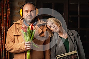 a ridiculous, funny photo of a couple - a man with a bouquet of tulips and a woman with a retro radio in a dark room