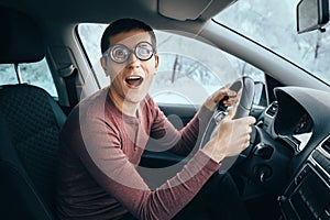 Ridiculous idiotic nerd driver in big eyeglasses holding the steering wheel and smiling to the camera. Concept of a