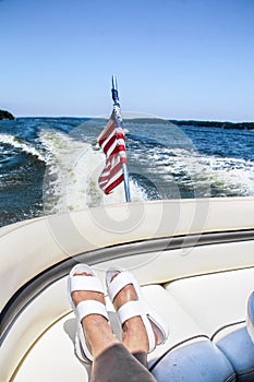 Riding in the back of the speedboat across the lake - womens feet with white sandals propped on curved seat with flag and wake and