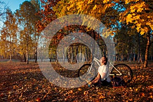 Riding bicycle in autumn forest. Young woman biker relaxing after exercising on bike. Healthy lifestyle