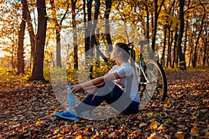 Riding bicycle in autumn forest. Young woman having rest after workout on bike. Healthy lifestyle