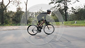 Riding a bicycle side follow view. Bearded man in black outfit on bicycle in the park. Out of the saddle pedaling.