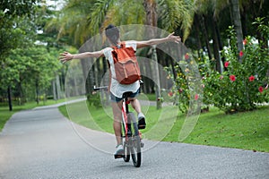 Riding a bike on sunny park trail with arms outstretched