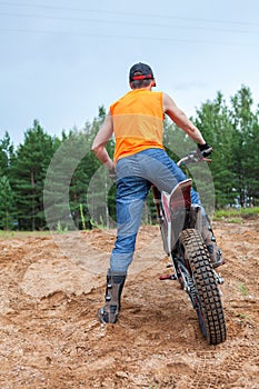 Riding motorcross motorcycle in sandy pit, Caucasian man dressed orange t-shirt standing with bike, rear view photo