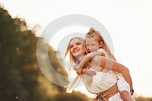 Riding on woman. Mother and daughter enjoying weekend together by walking outdoors in the field. Beautiful nature