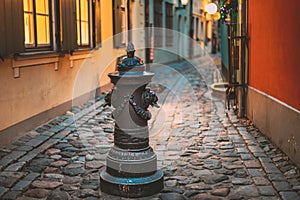 Riga, Latvia. Small Column Pillar Shaft Stake Pile With Lions Heads At Torna Street In Old Town. Narrow Street In photo