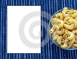 Rigati Pasta in a glass cup on a striped white blue cloth background with a side.White space for text and ideas.
