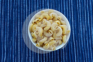 Rigati Pasta in a white cup on a striped white blue cloth background in the center.