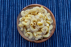 Rigati pasta in a wooden bowl on a striped white blue cloth background in the center.