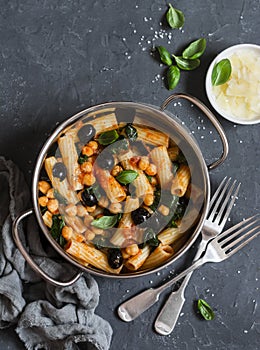 Rigatoni pasta with chickpeas, spinach and olives in a tomato sauce on a dark background, top view.