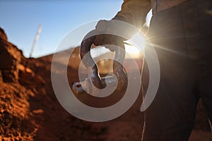 Rigger wearing a safety glove holding crane lifting 17 tone shackle with defocused crane at the back ground during sunset