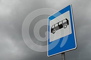 Right angled blue and white roadsign of bus stop against gloomy cloudy sky