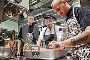 Right choice. Professional chef in apron holding a red meat and teaching his assistants how to choose it for cooking