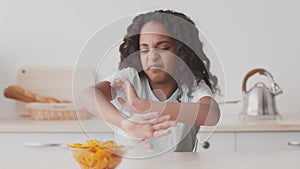 Right eating habits. Cute african american girl feeling disgust to bowl with chips, frowning face and moving it away