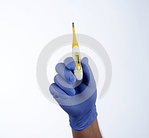 Right hand in blue glove holding a yellow medical thermometer