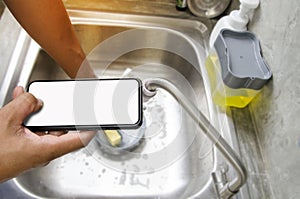 Right hand holding blank screen smartphone or mobile phone while washing dish in sink of kitchen.using technology for