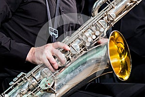 The right hand of the musician in a black shirt rests on a saxophone-baritone. Close-up.