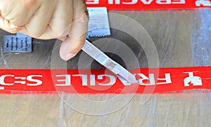 The right hand opening a box with fragile label using a small cutter,