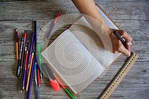 Right-handed woman holding pen while writing on small notebook on wooden rusty floor