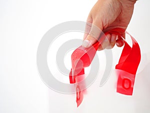 Hand holding red handle plastic shopping bag, white background