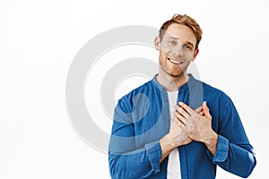 Right into my heart. Smiling attractive ginger guy holding hands on heart, being touched and happy, flattered by nice photo