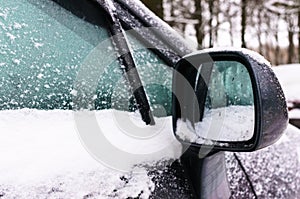 Right rear view mirror and side window of the car covered with snow