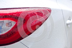 Right side rear red led taillight and part of rear side of a white car with small raindrops. Close up with details.