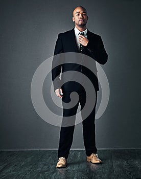 With the right suit, you can do anything. Studio shot of a handsome young businessman adjusting his tie against a gray