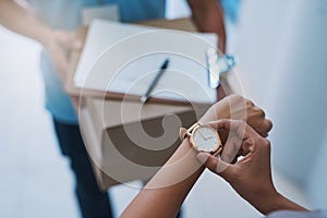 Right on time. an unidentifiable businesswoman checking the time on her watch as the courier arrives with a delivery.
