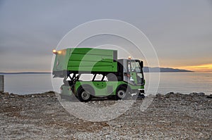Rijeka, Croatia February 2021. Garbage Day Pickup. Garbage truck caught in action emptyÃ¢â¬â¢s a trash bin in front of the sea.
