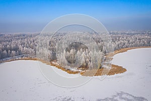 Rime and hoarfrost covering trees. Aerial view of the snow-covered forest and lake from above. Winter scenery. Landscape photo