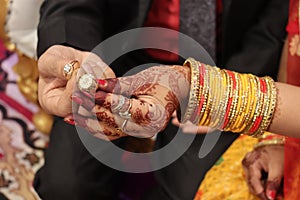 Ring ceremony and the wedding anniversary of the Hindu Indian couple holding gold ring. Royal bangles covering hands with traditio