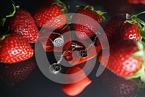 Ring and earrings with the symbol of bdsm lying among the strawberries on the black table top view