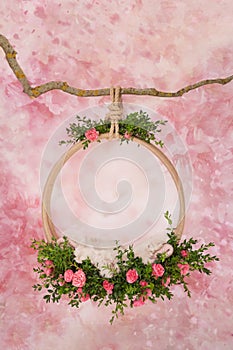 A ring of green twigs and pink roses hangs on a branch, for photos of newborn babies