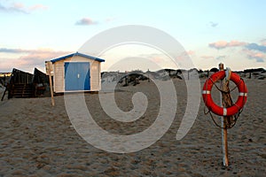 Ring-shaped lifesaver hang from a pole and a little white house with blue roof behind it