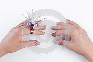 A ring with a small pillow for needles on a hand and scissors on a white background
