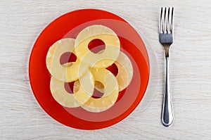 Rings of canned pineapple in red plate, fork on table