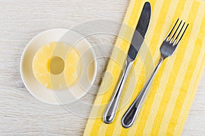Rings of canned pineapple in saucer, fork, knife on napkin