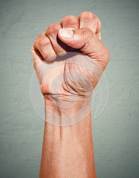 Riot protest fist raised in the air. Male clenched fist on dark grunge background.