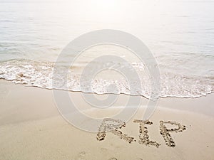 RIP, rest in peace, handwriting on nature sand tropical beach. Words written in sand against the sea in sunny day. Sadness concept