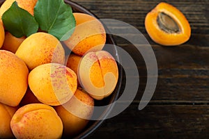 Ripe apricots and apricot leaves in a bowl on a wooden table. Fresh fruits from the home garden