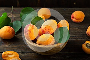 Ripe apricots and apricot leaves in a bowl on a wooden table. Fresh fruits from the home garden