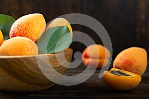 Ripe apricots and apricot leaves in a bowl on a wooden table. Fresh fruits from the home garden