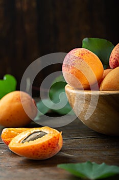 Ripe apricots and apricot leaves in a bowl on a wooden table. Fresh fruits from the home garden