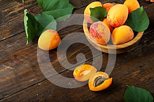 Ripe apricots and apricot leaves in a bowl on a wooden table. Fresh fruits from the home garden
