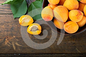 Ripe apricots and apricot leaves in a bowl on a wooden table. Fresh fruits from the home garden