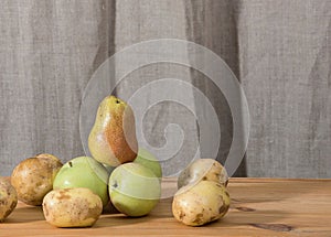 Ripe autumn pears and green apples are stacked in a large pyramid on a wooden rustic table.
